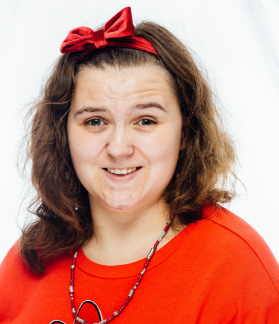 smiling brunette woman in a red shirt with a red bow in her hair.