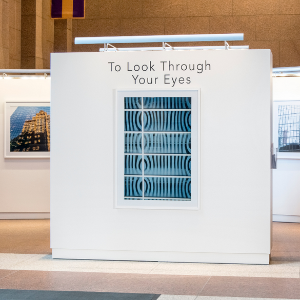 art displayed on free standing walls at back of america. the center wall has the text 'to look through your eyes' and a blue print.