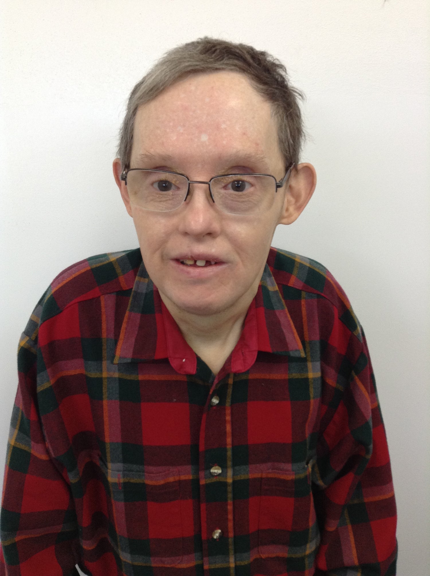 Male with grey hair wearing glasses and a red plain button down shirt.