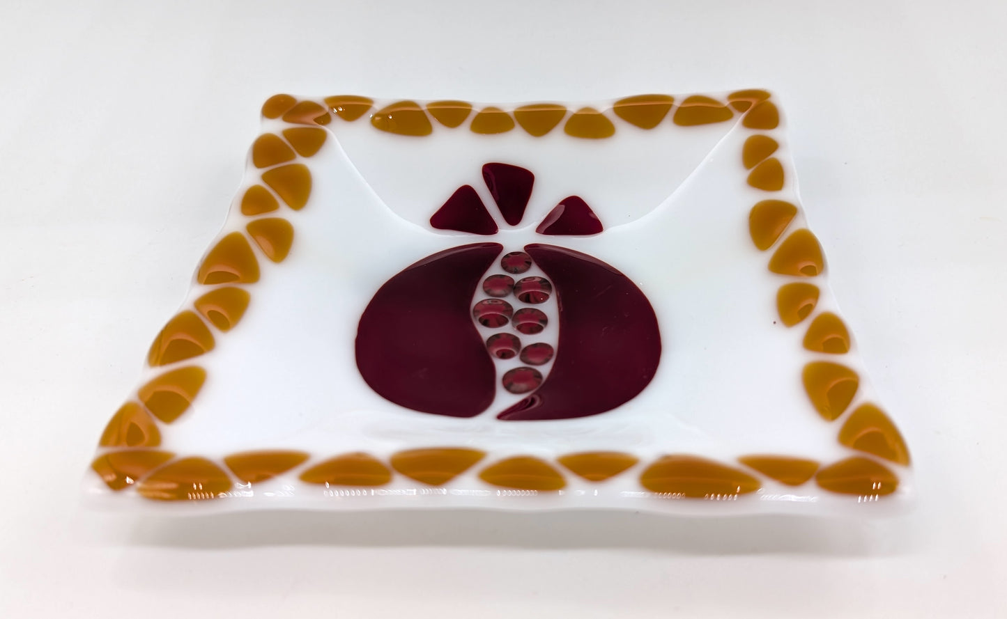 glass square plate with pomegranate design in the center and honey triangles along the edges