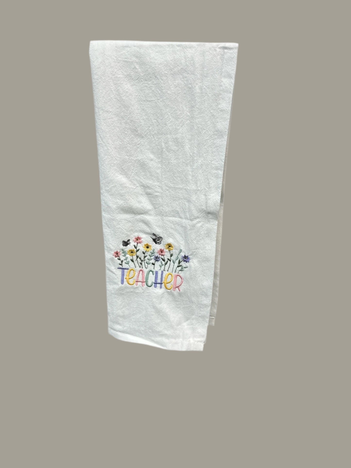 Embroidered White towel with Teacher saying and flower decorations around.