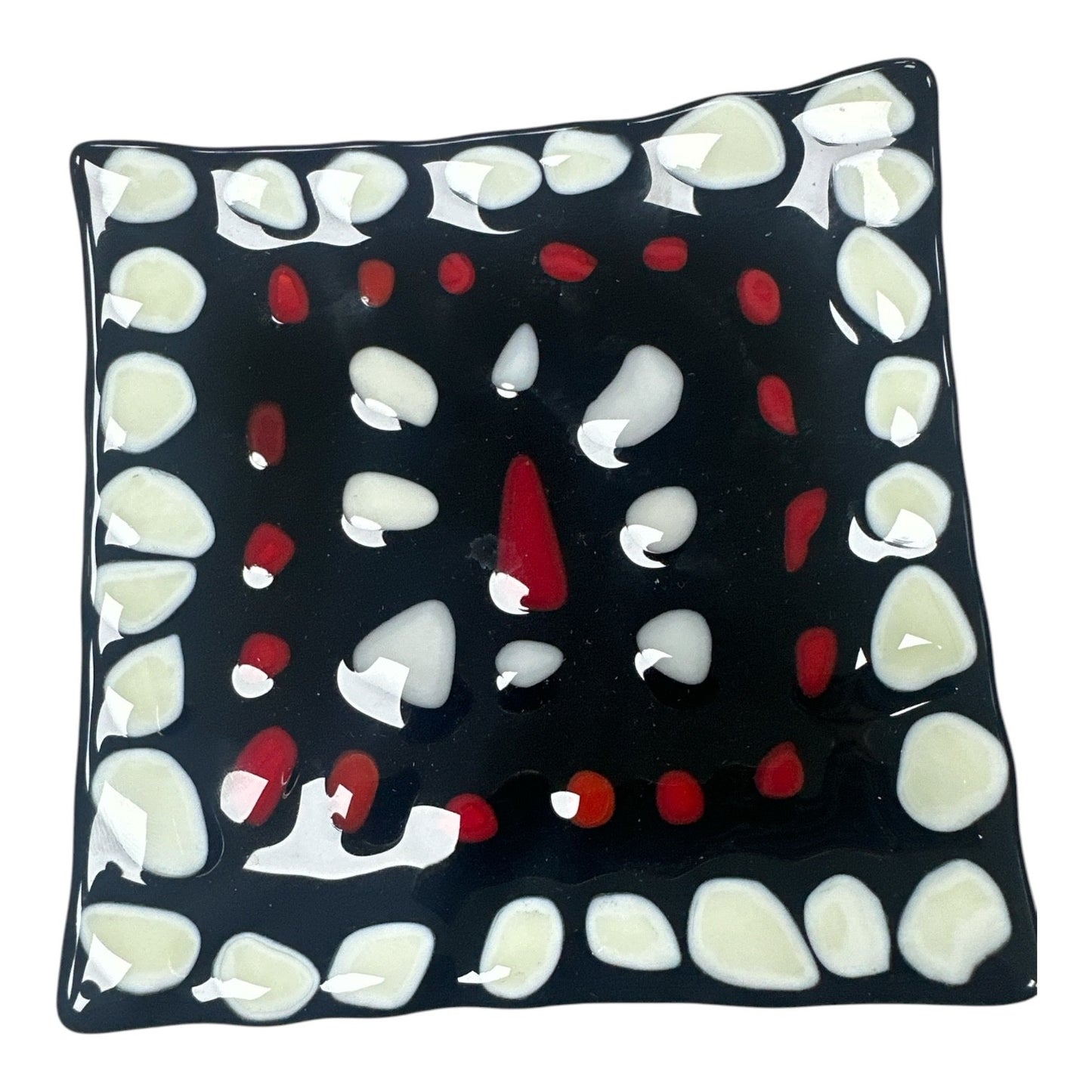 This is a square, black fused-glass decorative dish featuring a bold border of white pebble-like shapes that frame an inner square of small red accents and a central abstract arrangement of white and red glass