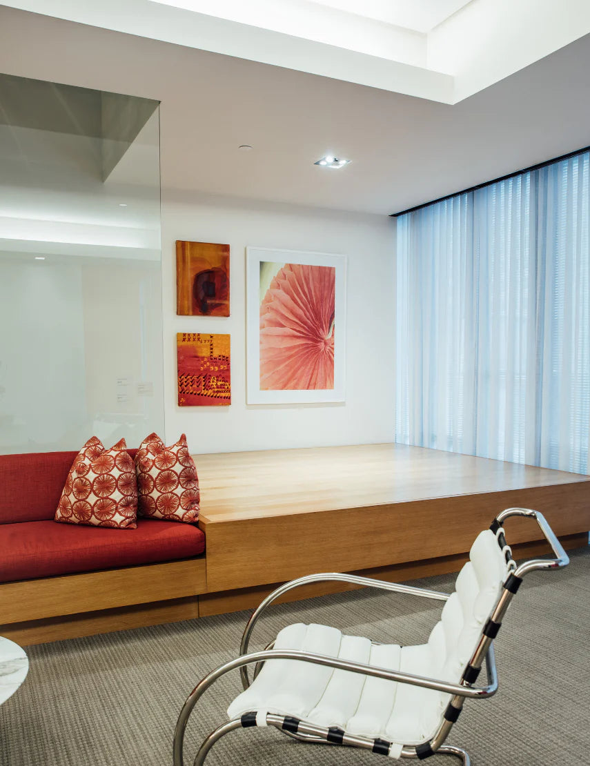 an office with a white chair, a red sofa, and 3 celebration company artwork pieces on the wall.