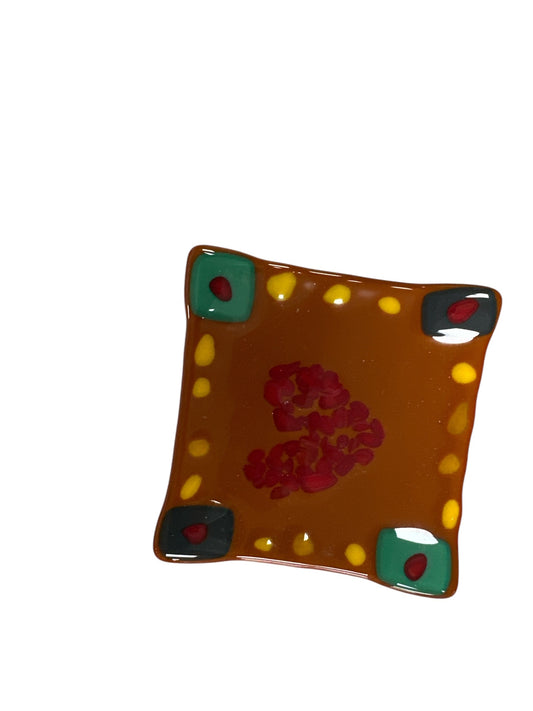 Fused brown glass with yellow dots around; black and red on diagonal corners and aqua and red on diagonal corners.