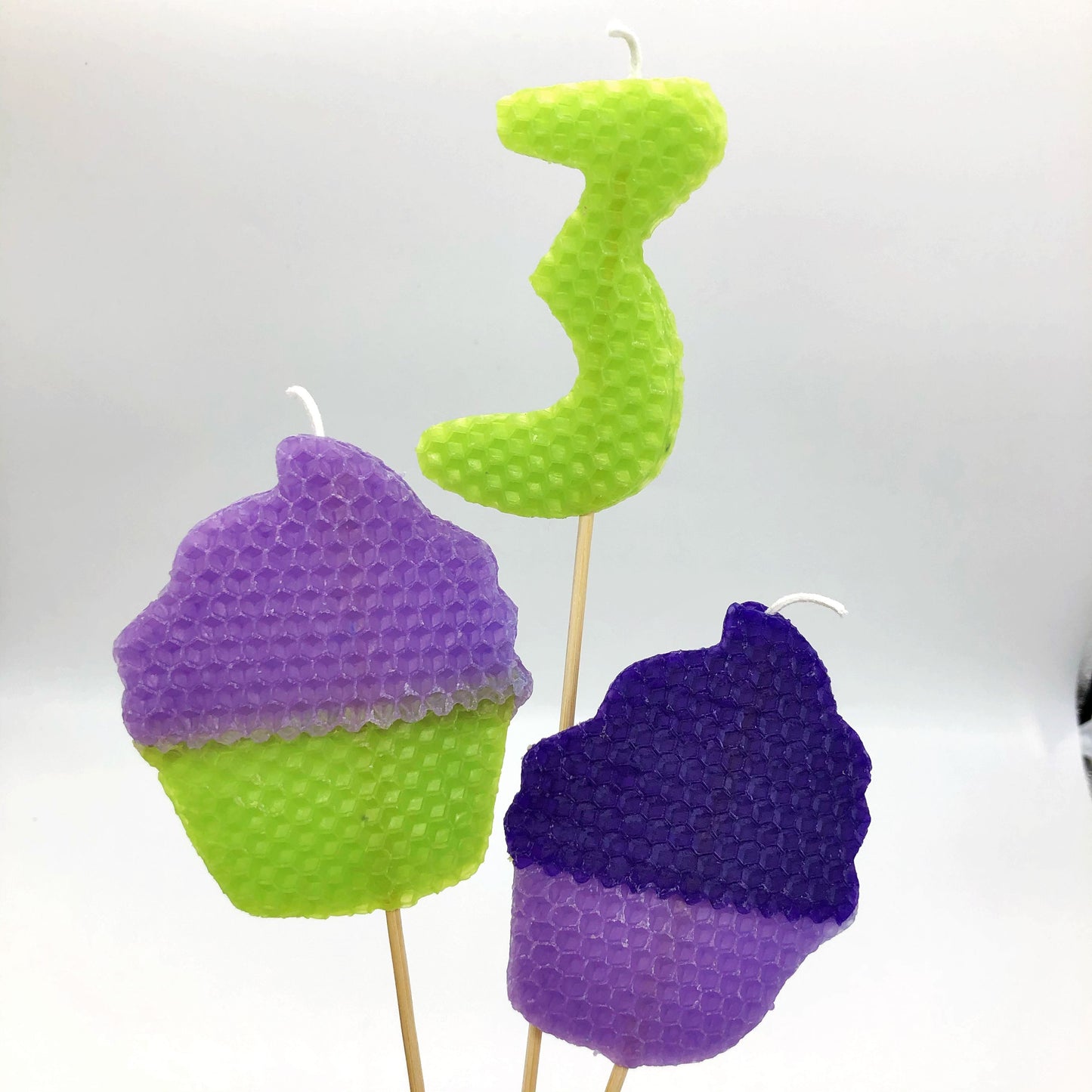 Pink and green beeswax cupcake candle, lime green number three beeswax candle, and dark and light purple cupcake beeswax candle
