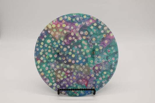 Glass cutting board with blue, green and purple swirl background with yellow, green and pink dots