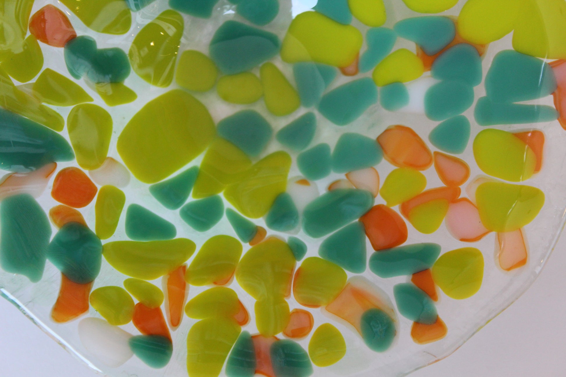 This up-close photo is of a glass bowl with dark green, yellow, and orange irregular/abstract shapes.