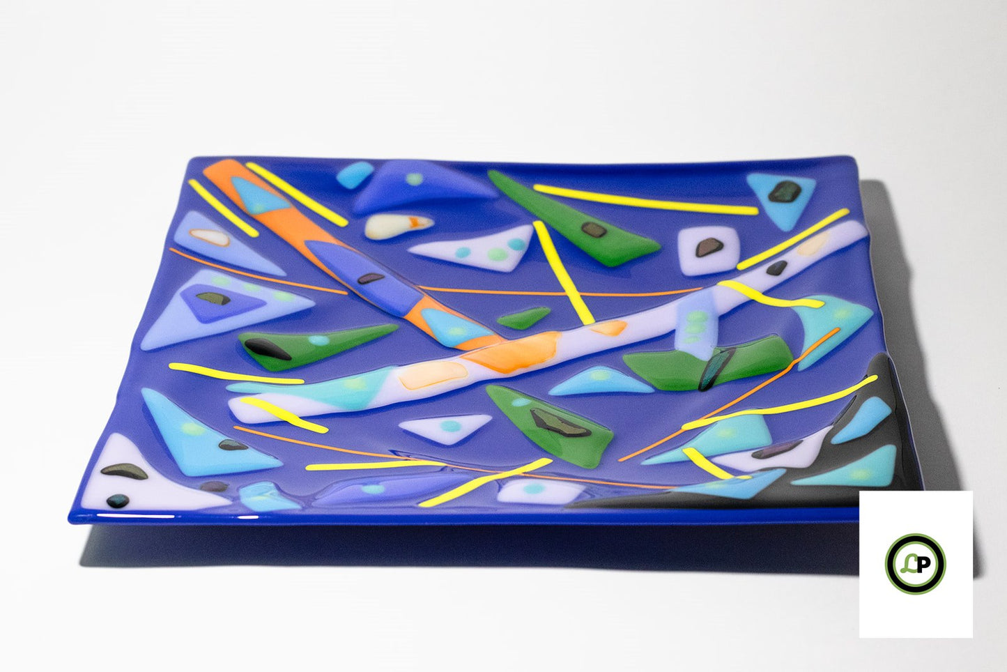 Blue glass dish with geometric shapes in blues, oranges, greens, and black.