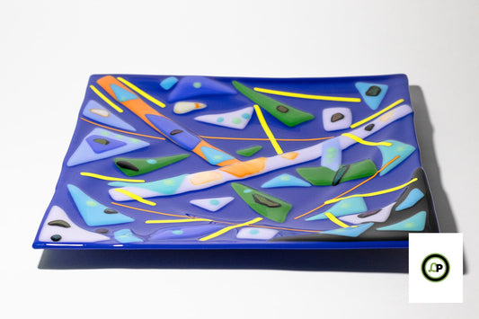 Blue glass dish with geometric shapes in blues, oranges, greens, and black.