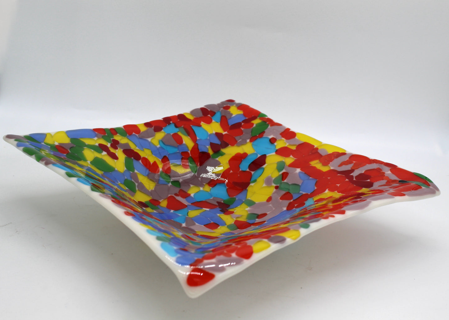 White glass square bowl completely covered in transparent chunks of bright colorful glass of reds, yellow, blues, green, and purple