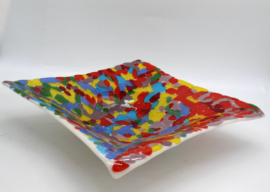 White glass square bowl completely covered in transparent chunks of bright colorful glass of reds, yellow, blues, green, and purple