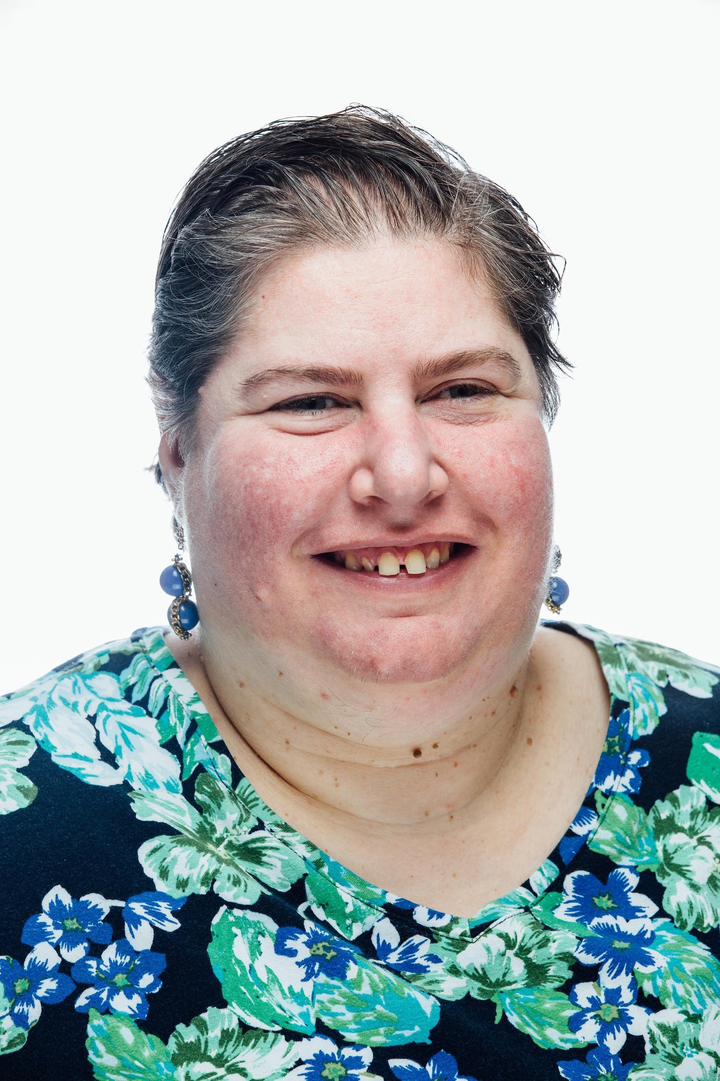Smiling woman wearing blue earrings and green and blue floral blouse