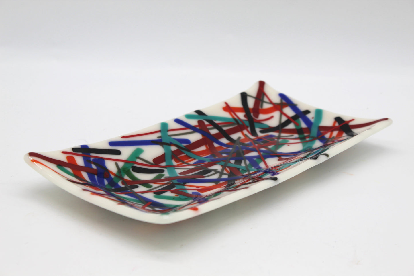 This is a piece of fused glass that is white with muticolored linked in abstarct form. Colors include: black, blue, light blue, red, and orange