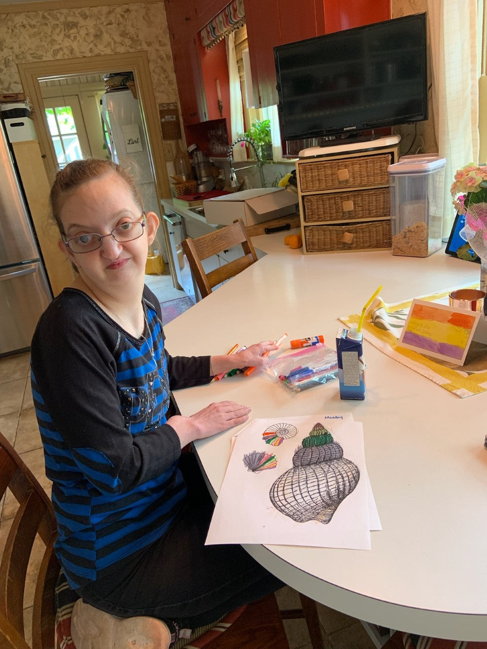 Female participant working at home during the pandemic on art exercises.  She is sitting at her kitchen island with the sun shining on her face.