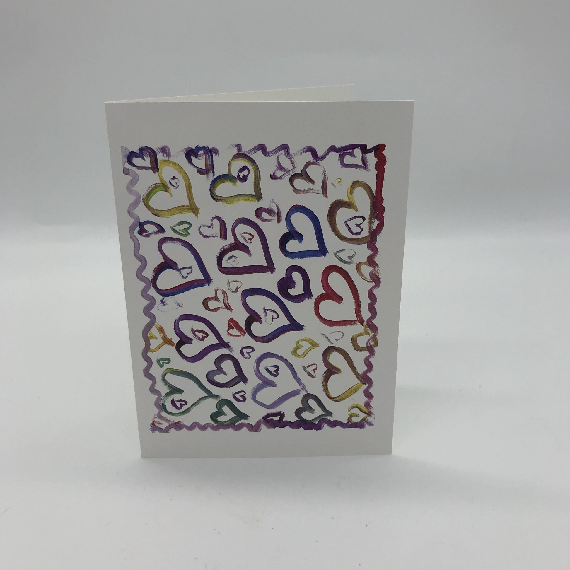 White greeting card with about a dozen large water colored hearts in blues, purples, and yellows.  There are several smaller hearts of varying sizes all around those larger hearts and a squiggly line in shades of purple and red framing all of it.