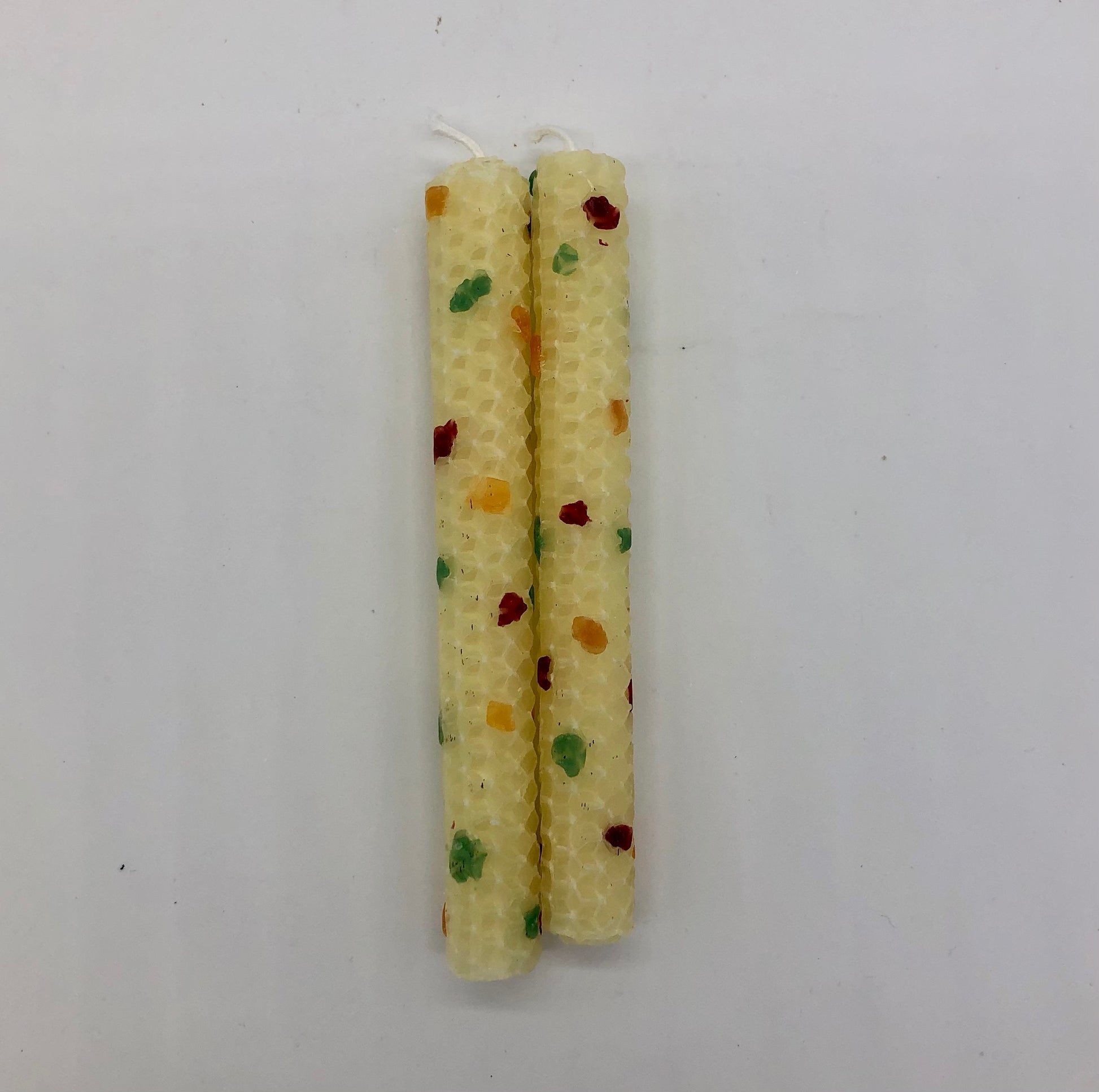 Two white shabbat candles with dots of color in green, orange, green and maroon..