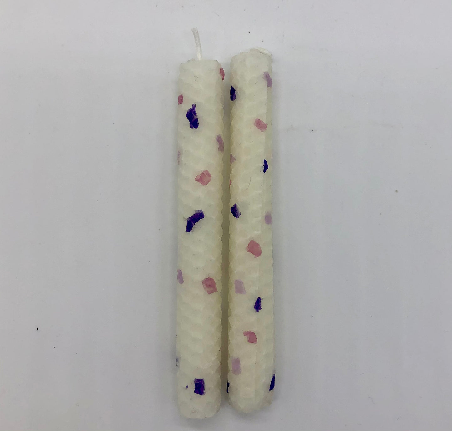 Two white shabbat candles with dots of color in purples and pink.