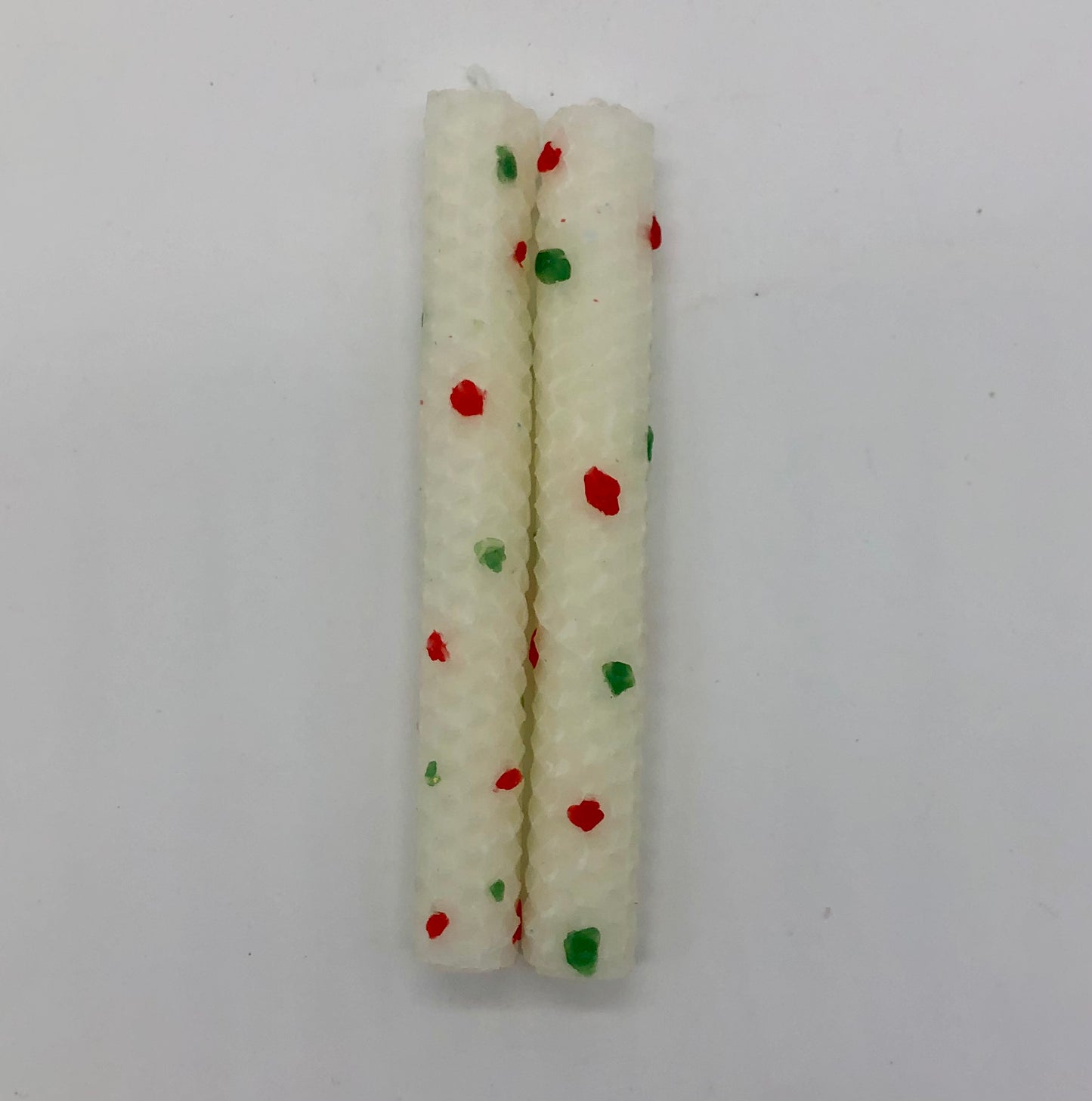 Two white shabbat candles with dots of color in red and green.