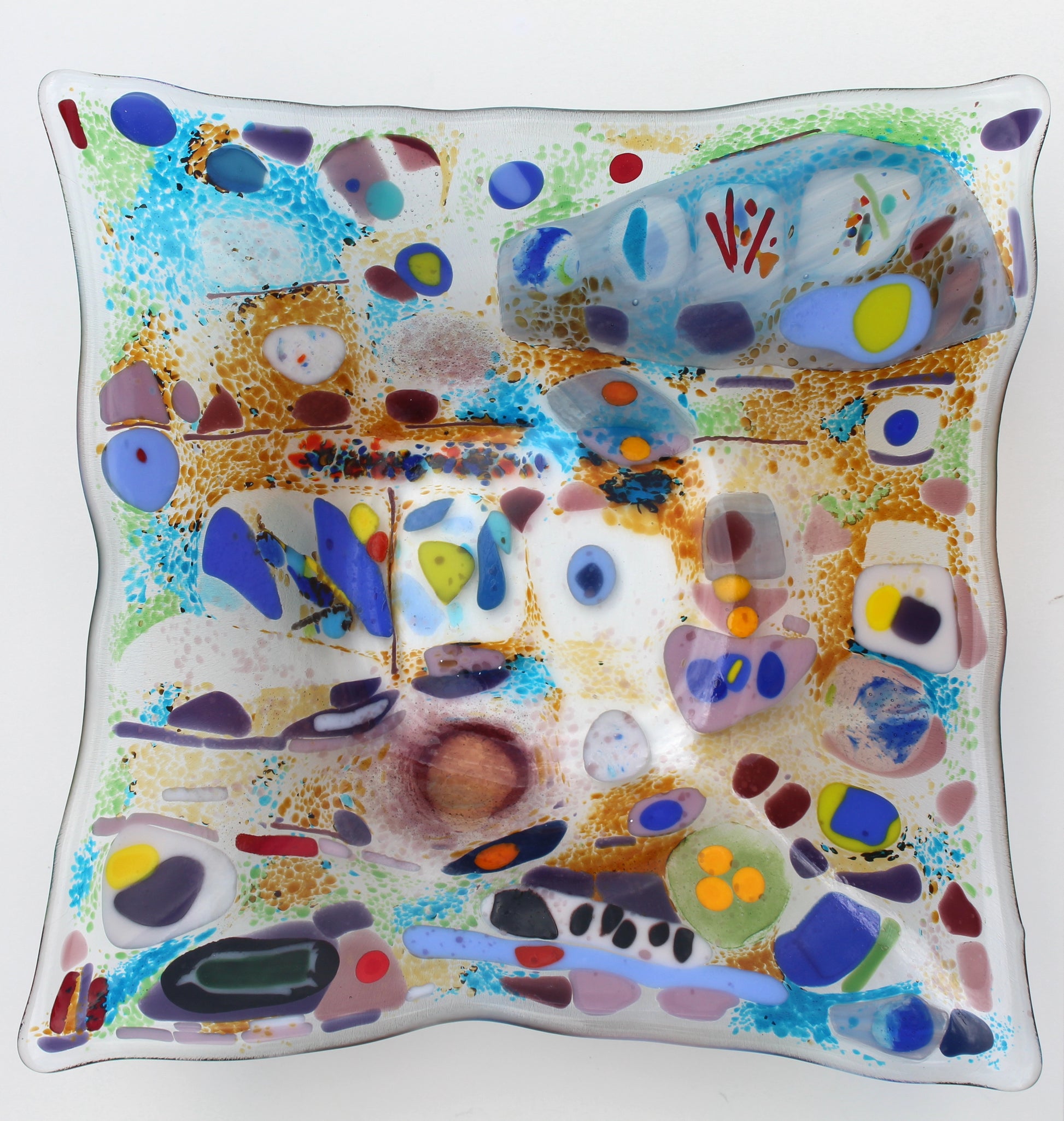 This is a piece of glass art with severl abstract shapes. The colors include blue, purple, red,orange, and green. It is a very unique design