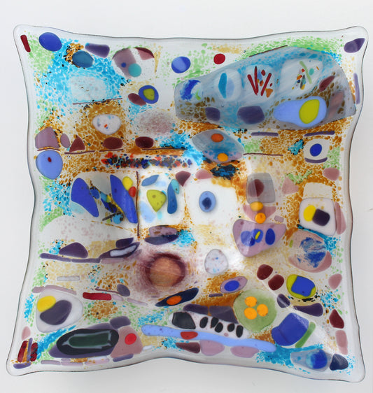 This is a piece of glass art with severl abstract shapes. The colors include blue, purple, red,orange, and green. It is a very unique design