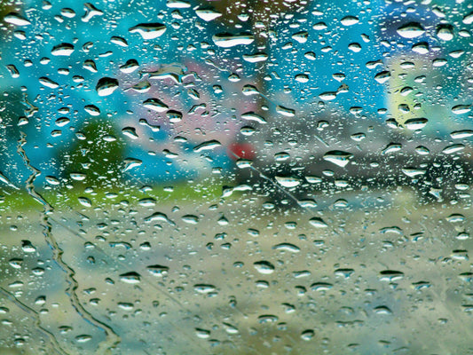 This is a photo of raindrops on a glass, with blurry landscape in the background