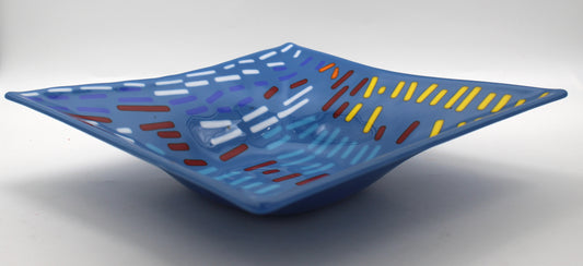 This is a blue square glass art with multicolored dashes in red, white, orange and yellow.