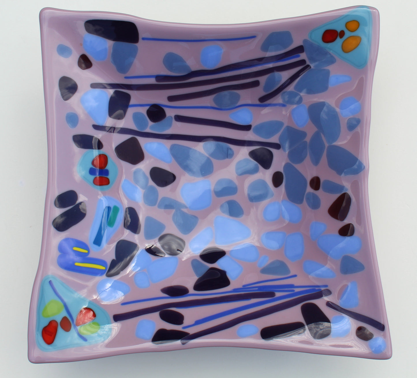 This is a square purple glass art with abstract black, blue, yellow and red shapes