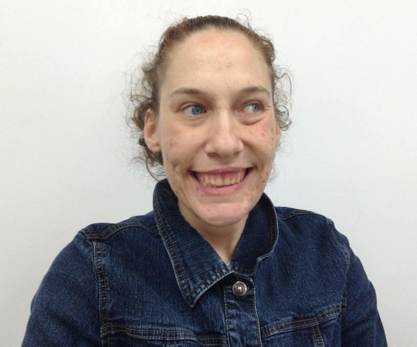 Young lady with light brown curly hair pulled back. Smiling wide so teeth is showing , wearing a blue jean jacket