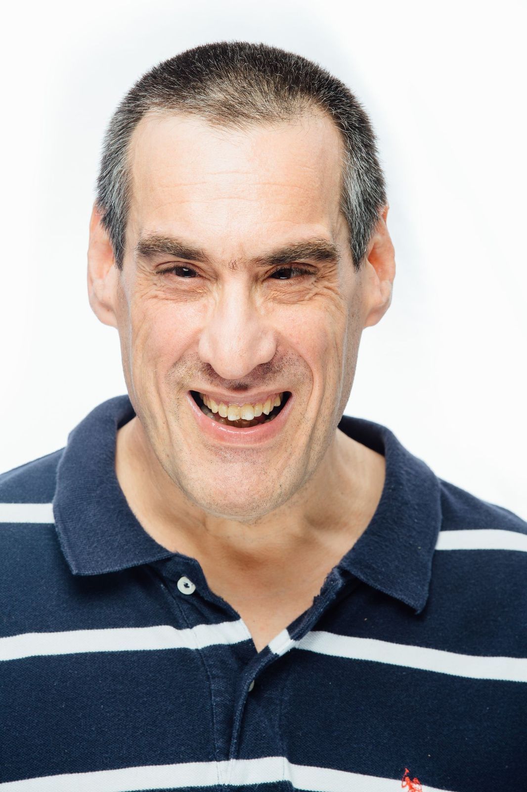 man with a buzz cut, smiling. wearing a blue and white striped shirt