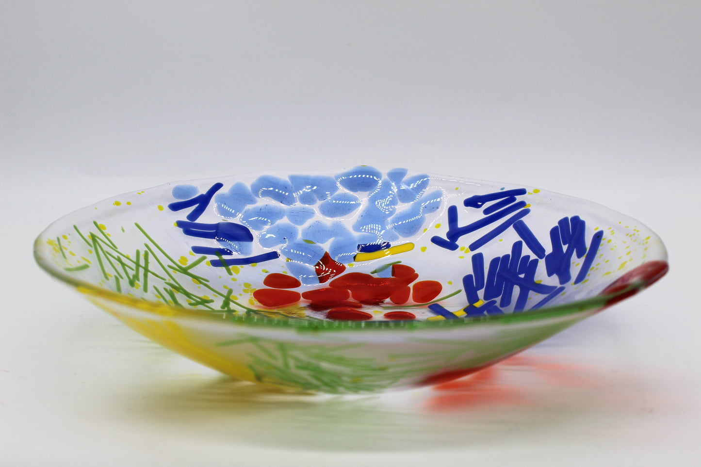 This is a clear circular glass art with blue, green and yellow lines. It has several red and blue abstract shapes as well