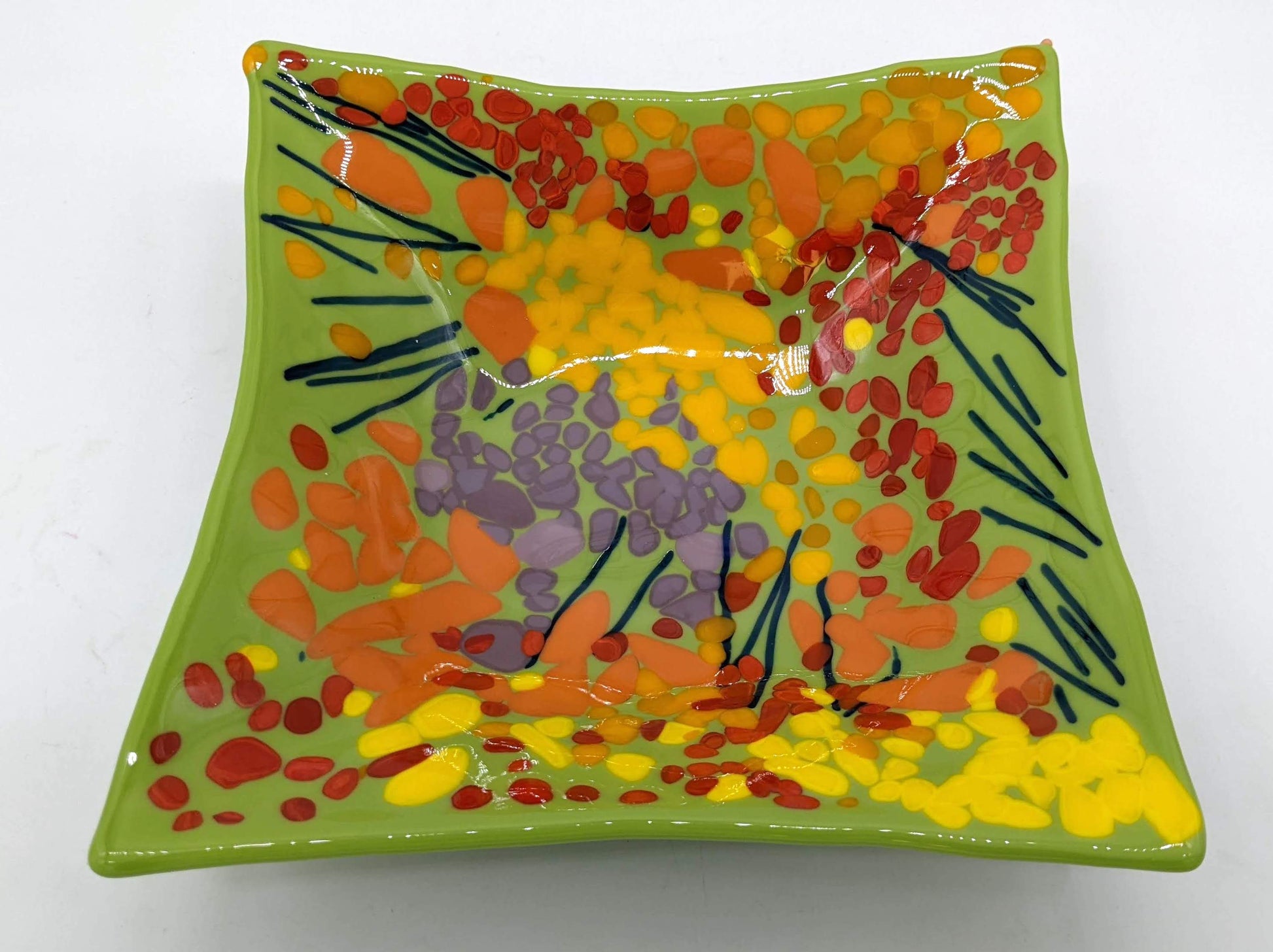 green glass square bowl covered in red, yellow, orange, and purple dots with navy lines