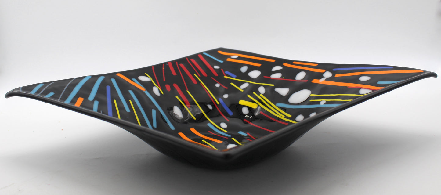 This is a black square glass art with multicolored lines in red, yellow, blue, and orange. It has white dots overlaying it