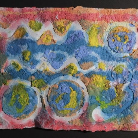 Highly textured handmade paper with the edges red and the center a series of blues with highlights of yellow. Amongst the colors are waves and circles that are embossed and white