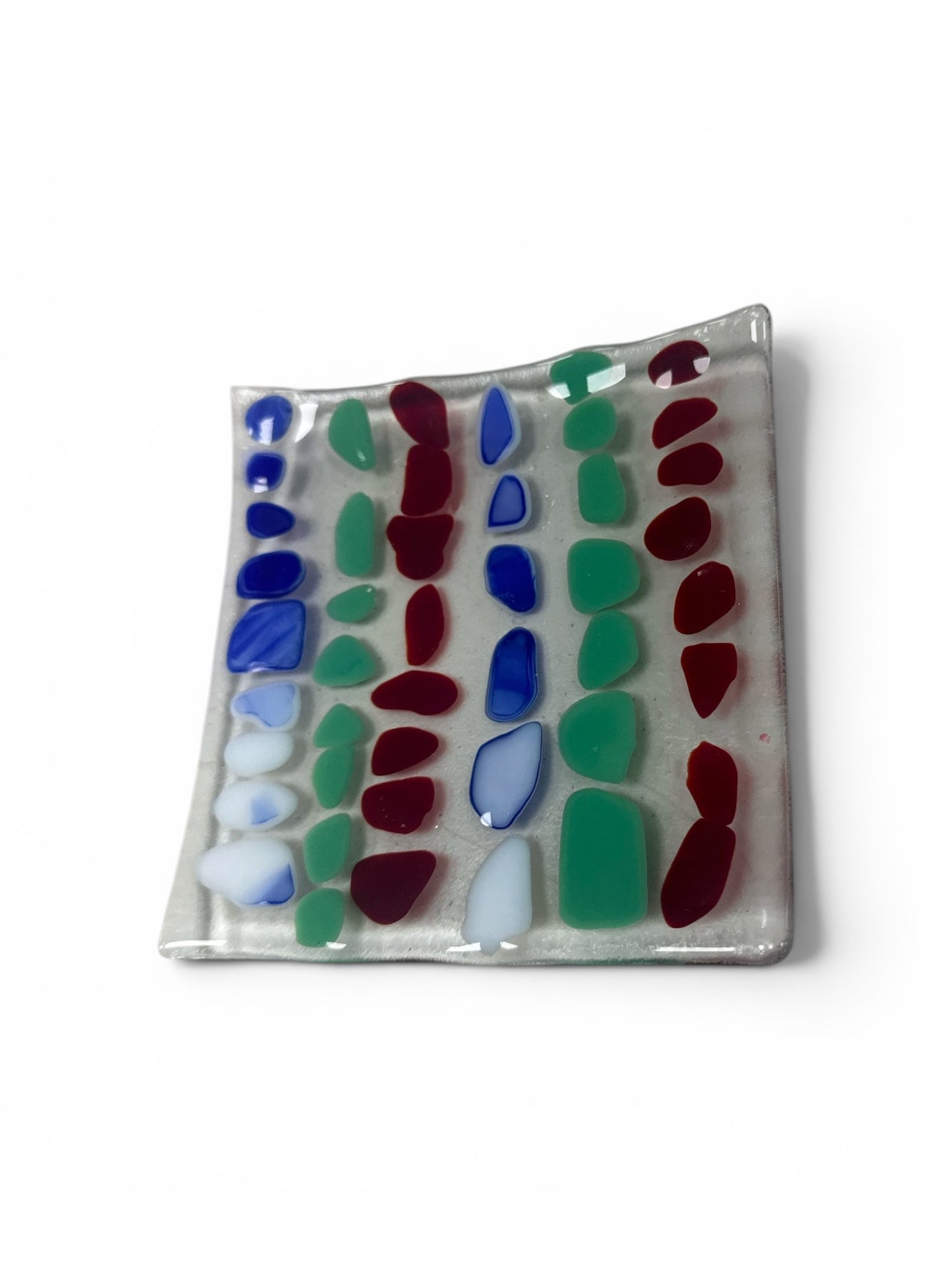 Handcrafted fused glass dish. It features rows of colorful, pebble-shaped glass accents in vibrant blue, green, and deep red set against a clear base.