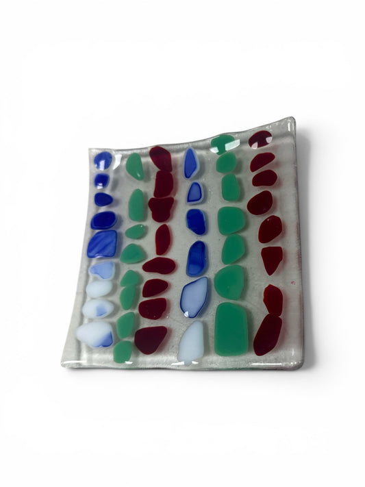Handcrafted fused glass dish. It features rows of colorful, pebble-shaped glass accents in vibrant blue, green, and deep red set against a clear base.