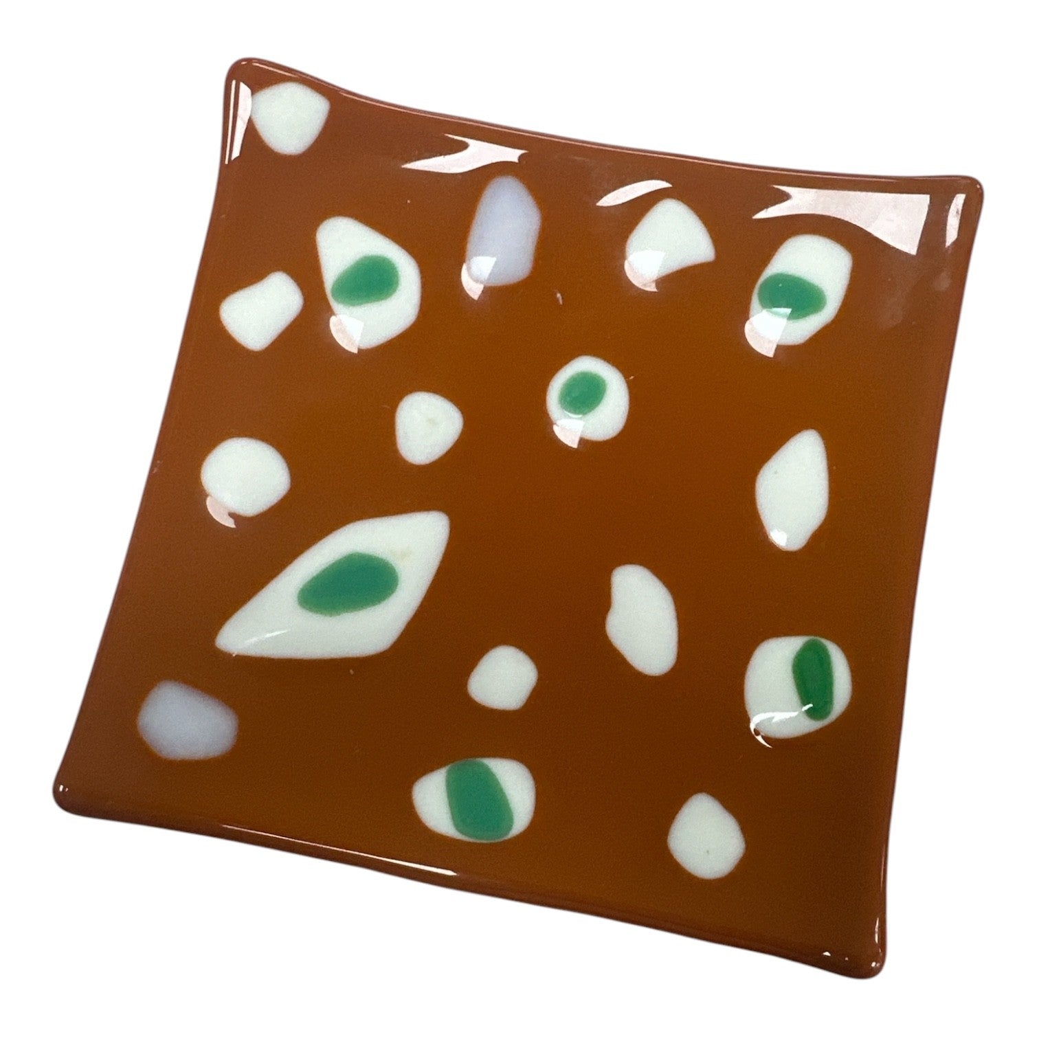 This is a square, warm brown fused-glass decorative dish scattered with an organic, abstract pattern of smooth white shapes, several of which feature vibrant green centers.