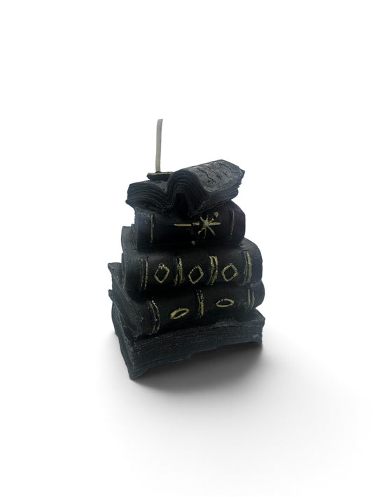 A miniature stack of black book candles with gold-detailed spines topped with an open book wick.