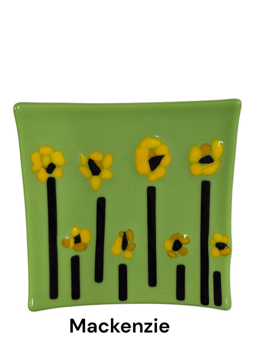 Handcrafted fused glass art tray, it features a cheerful garden design with bright yellow flowers atop tall, slender black stems, all set against a vibrant spring-green background.

Medium: Fused Glass

Size: Approximately 6" x 6"

Year: 2026