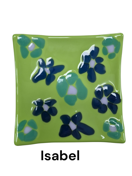Handcrafted fused glass art tray, it features a charming floral design with stylized blossoms in deep blue and teal against a vibrant, grassy-green background.

Medium: Fused Glass

Size: Approximately 6" x 6"

Year: 2026