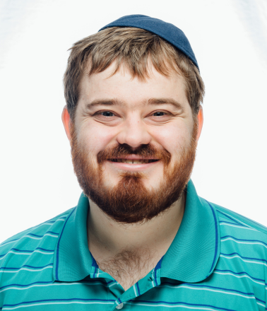 Smiling man with a bear wearing a kippot and teal striped polo shirt.