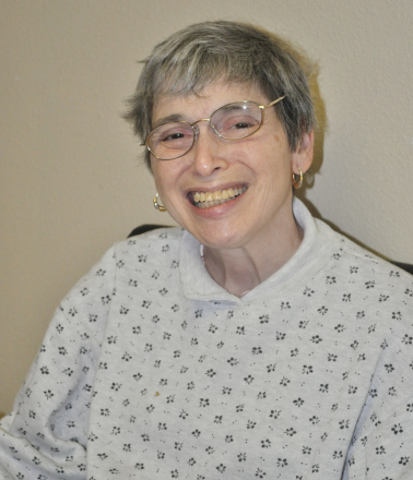 Smiling older woman wearing glasses and a white sweater.
