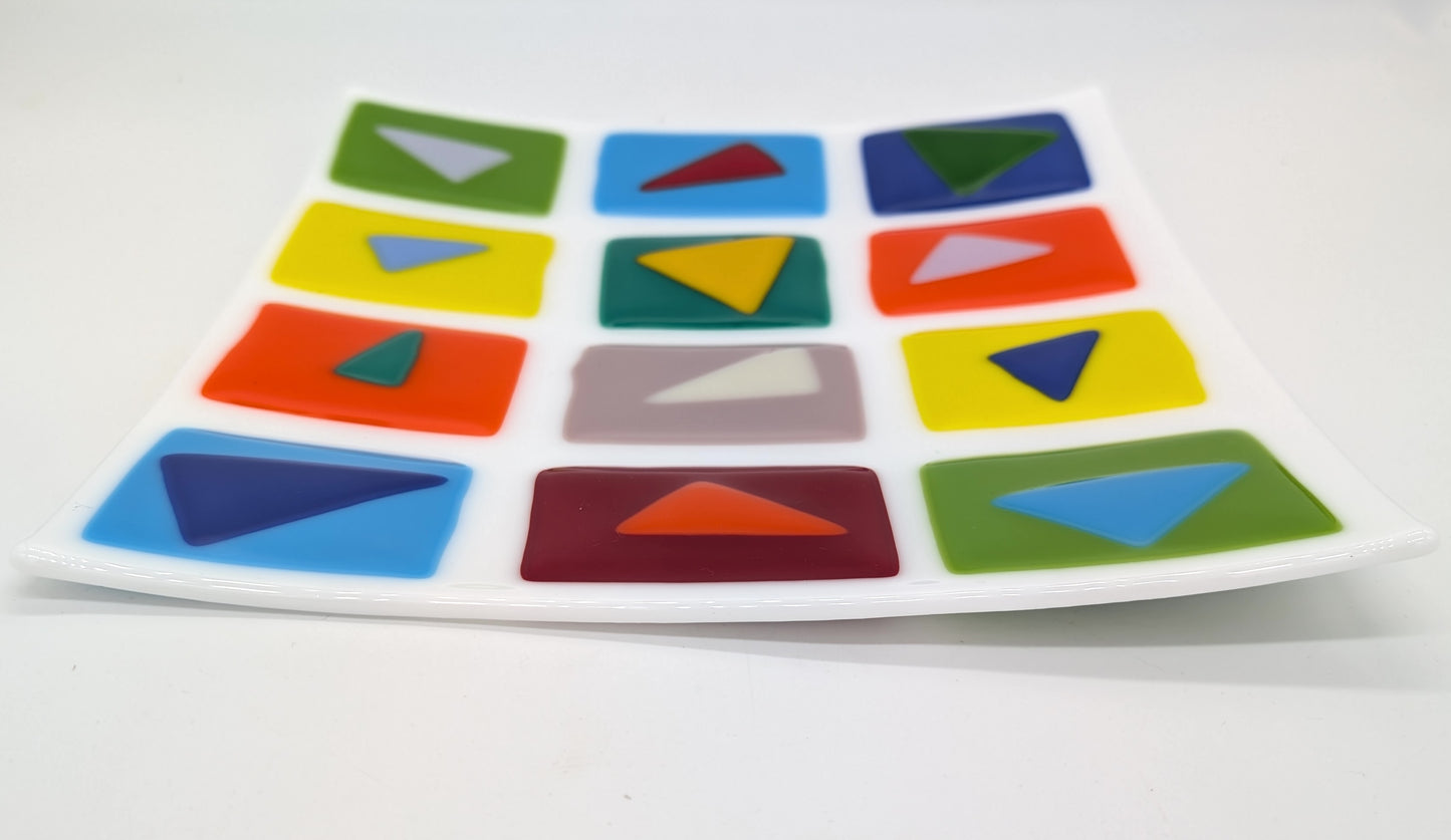 white square glass plate with a variety of bright colored squares arranged in a grid with contrasting triangles on top