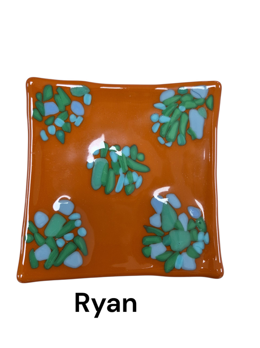 Handcrafted fused glass art tray, it features an earthy, warm orange base accented by clustered mosaic patterns of cool-toned teal and light blue glass shards.