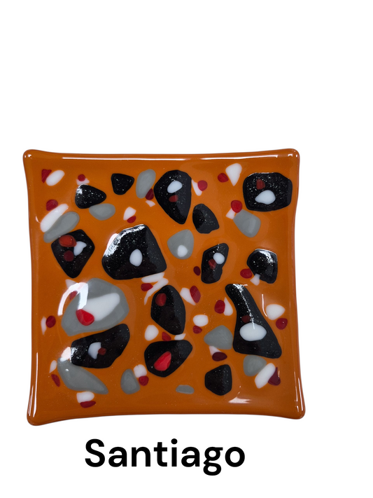 Handcrafted fused glass art tray, it features a bold, high-contrast design with an earthy orange background, punctuated by an abstract scatter of black, grey, white, and red glass accents.

Medium: Fused Glass

Size: Approximately 6" x 6"

Year: 2026