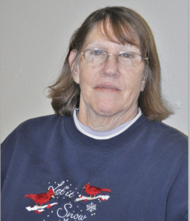 Older female wearing glasses and a blue sweatshirt that reads "let it snow".