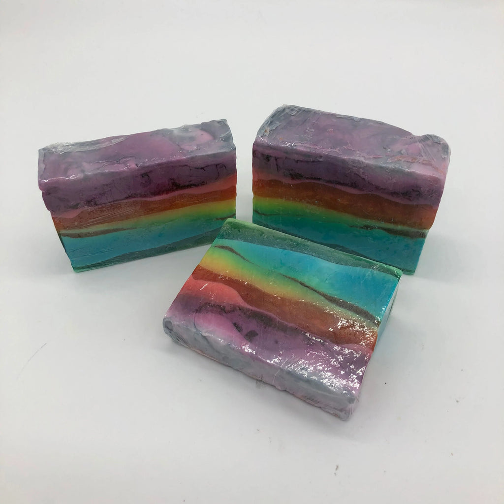 Three colorful cars of homemade rainbow soap with purple pink red blue and green stripes