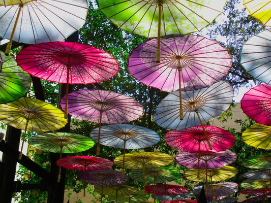 Photograph of a series of colorful paper umbrellas in the sky with the sunlight shinning through