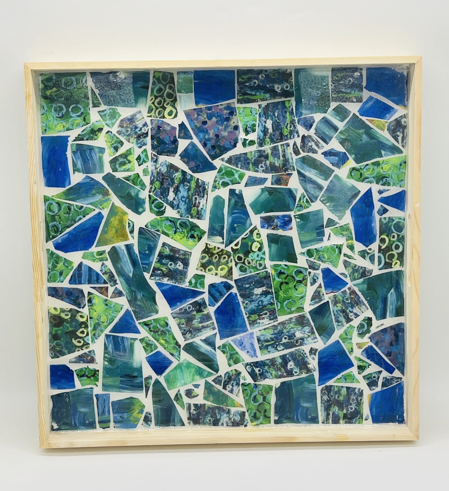 square wooden tray filled with broken mosaic tiles filled with shades of blue and green