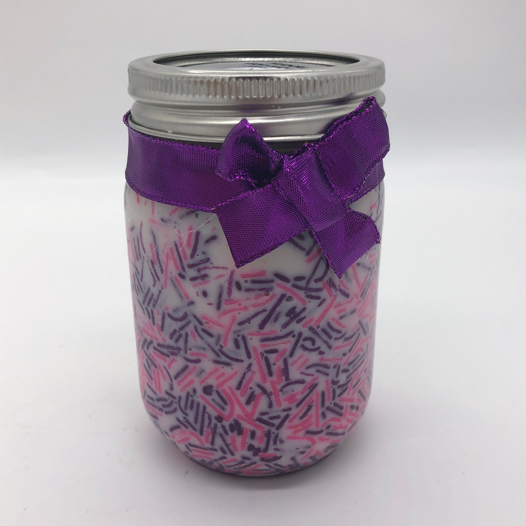 Canning jar with a white candle inside, pink and purple candy sprinkles decorating the sides.  Purple metallic bow on the outside.