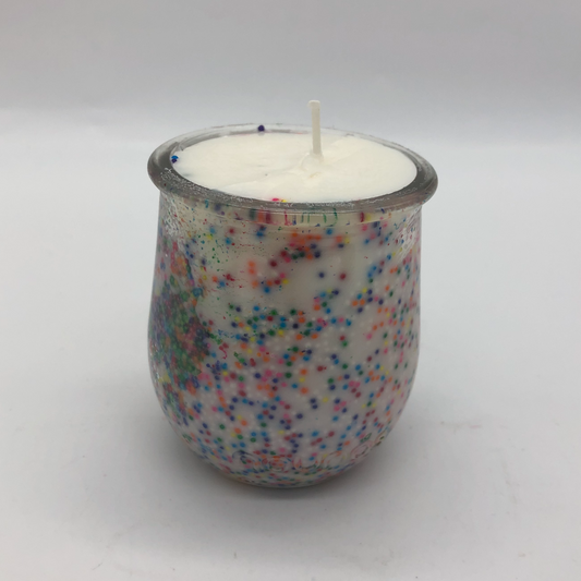 Small glass jar with white candle inside.  There are colorful sprinkles on the inside of the jar.
